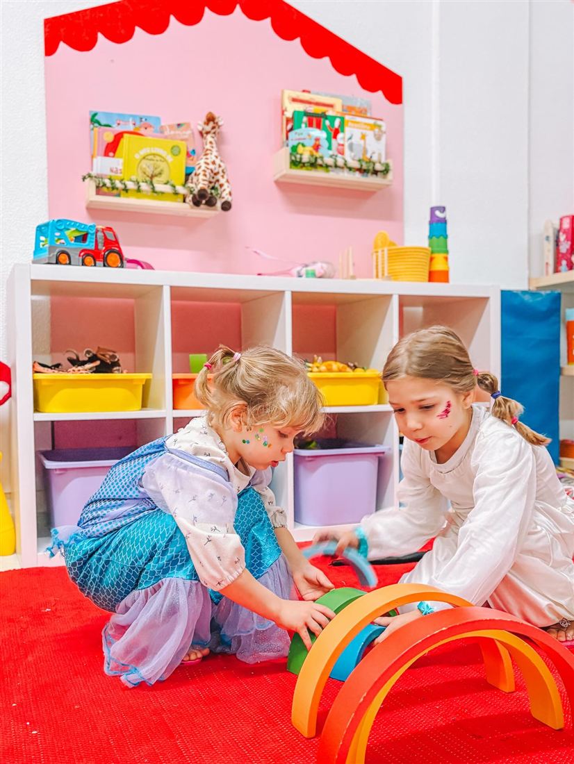 Duas meninas a brincar com um arco-íris de madeira no espaço kids